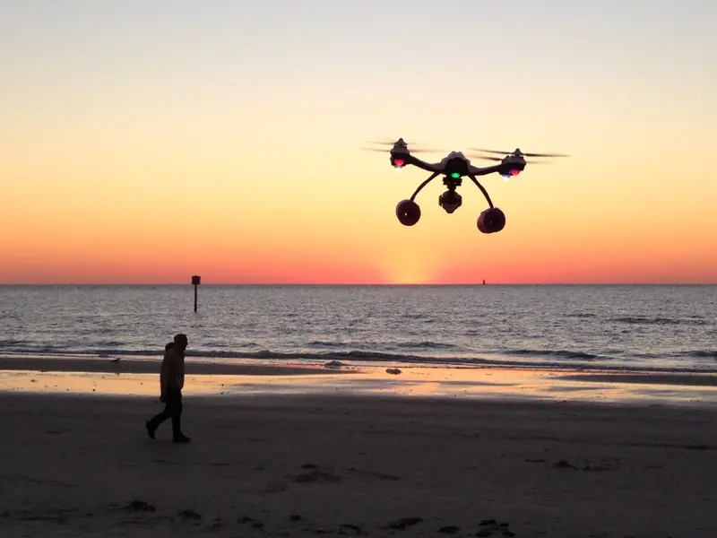 Drone pilot launching drone at sunset over the water — FAA-certified aerial survey