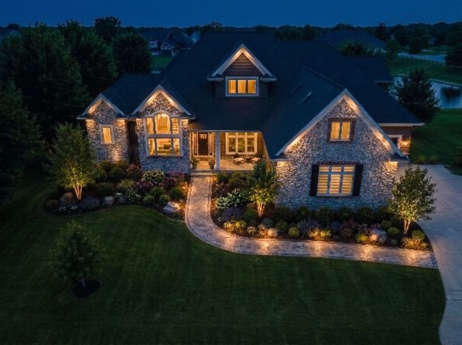 Robins Iowa front yard night lighting concept by Darin Chamberlin — landscape uplighting on stone facade, path lighting along walkway, warm interior glow, and downlighting on planting beds